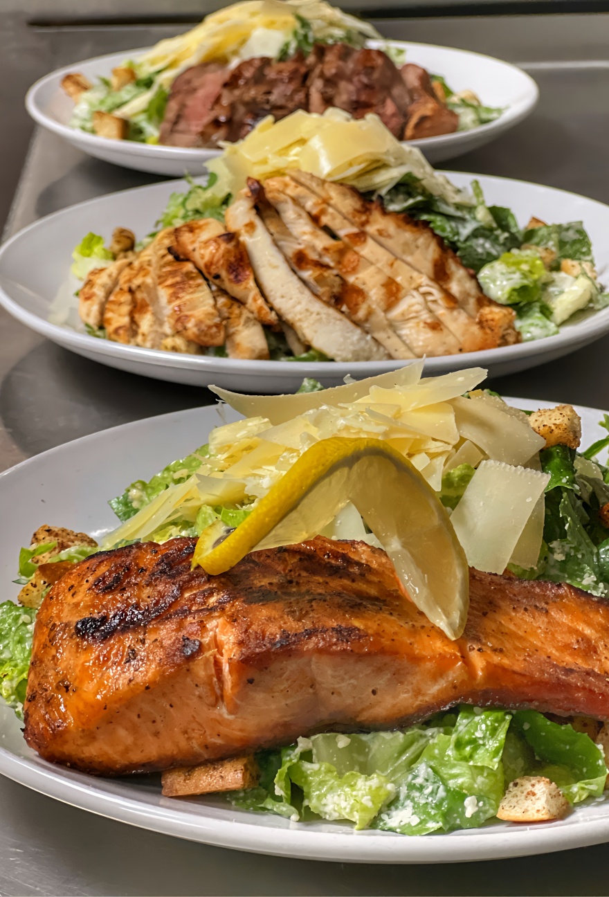 Three different caesar salads one topped with salmon, one with chicken, and one with steak