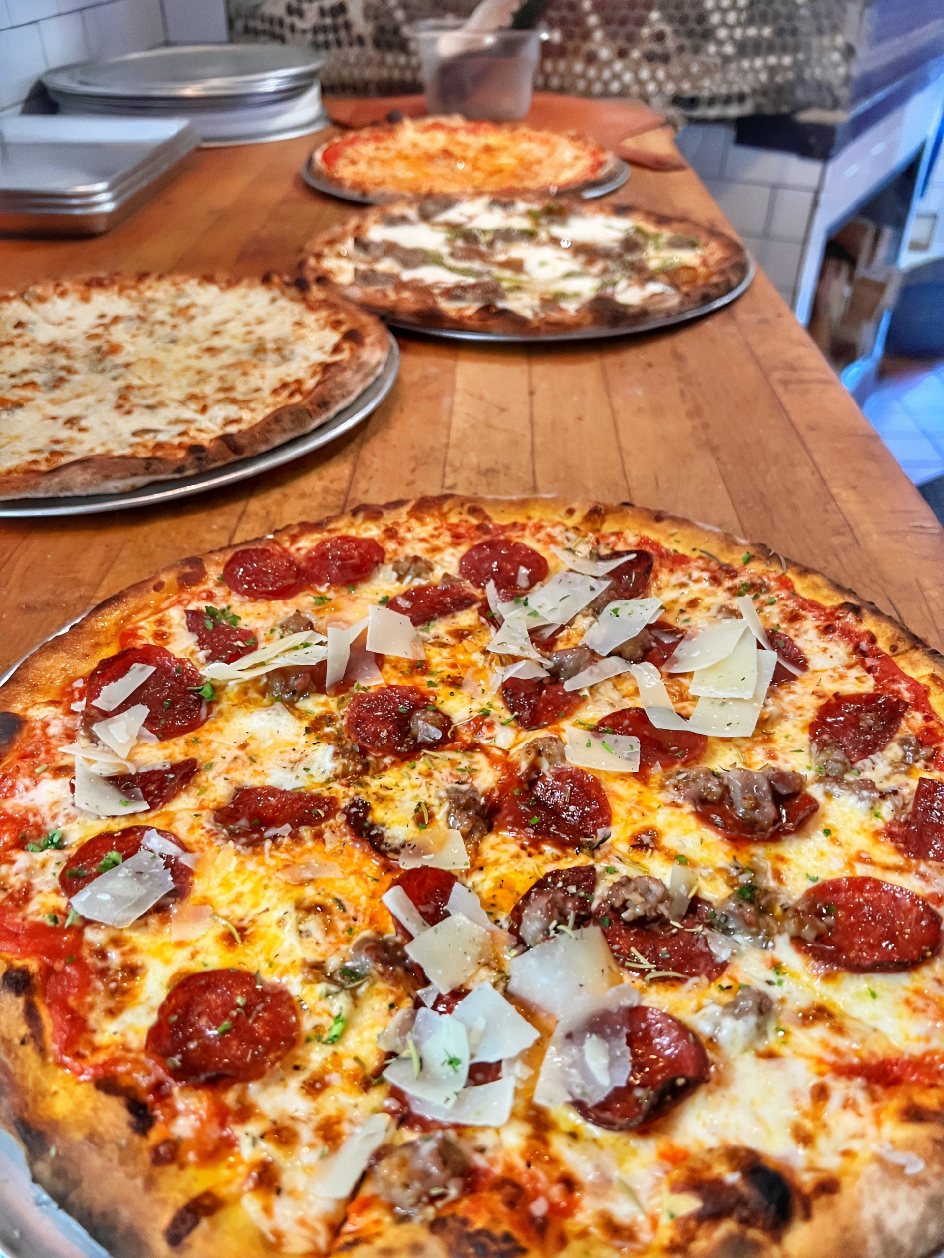 Wood-fired pizzas with a pepperoni pizza topped with shaved parmesan in focus